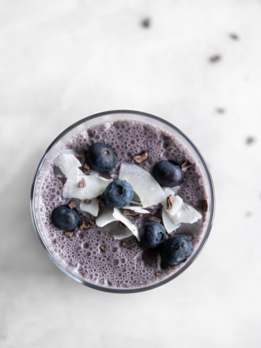 A glass of blueberry coconut smoothie with fresh berries and coconut on top