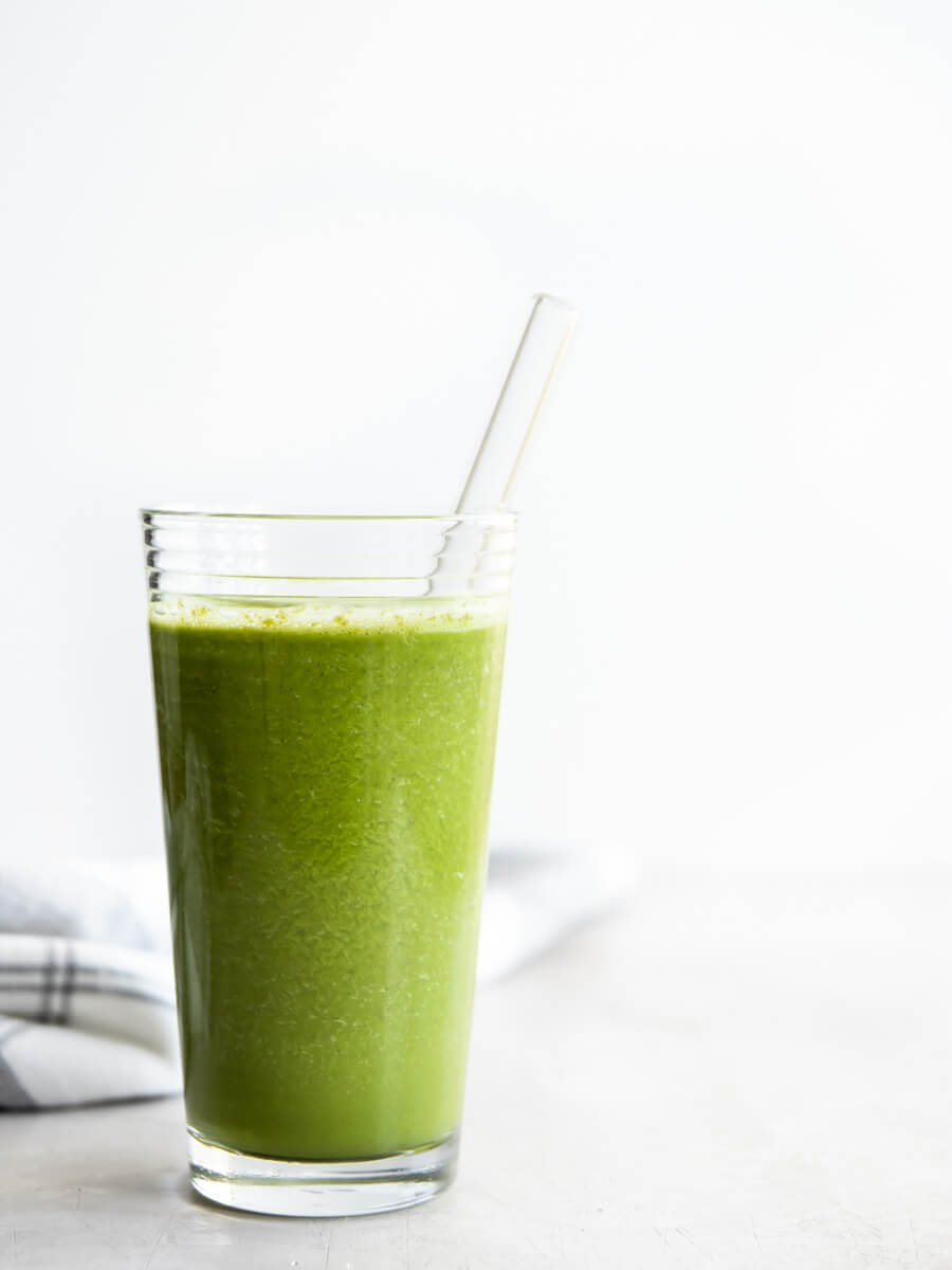 A glass of kale pineapple smoothie with a glass straw. 