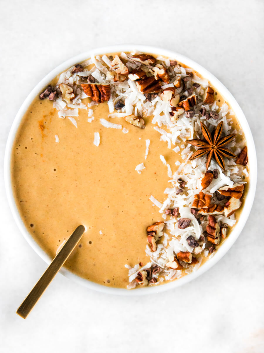 A bowl of pumpkin smoothie with toppings and a spoon.