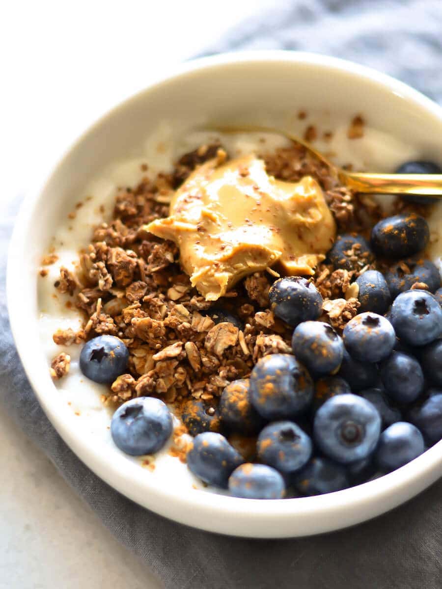 A bowl of yogurt topped with blueberries, granola, and nut butter. 