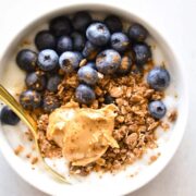 A yogurt bowl topped with granola, nut butter, and fresh blueberries.