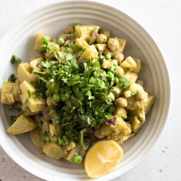 A bowl of masala potato salad topped with fresh cilantro and a wedge of lemon