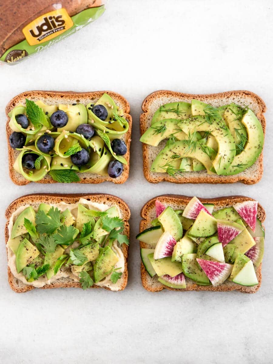 Four avocado toasts, each with different toppings, next to a loaf of gluten-free bread.