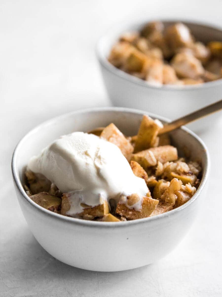 Bowl of walnut apple crisp with a scoop of melted ice cream on top