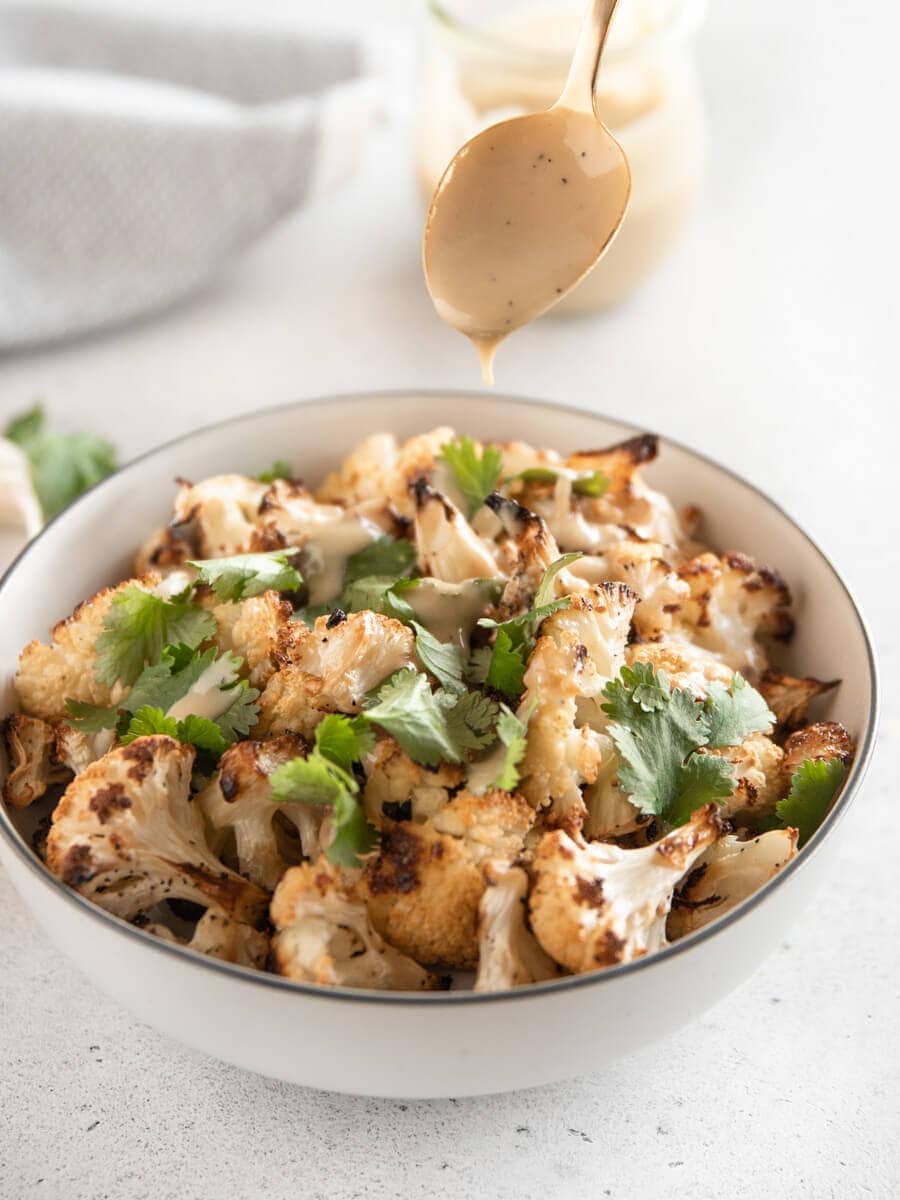 Garlic Roasted Cauliflower being drizzled with tahini sauce