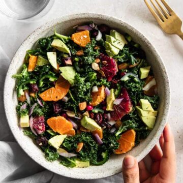 Bowl of kale citrus salad with hand