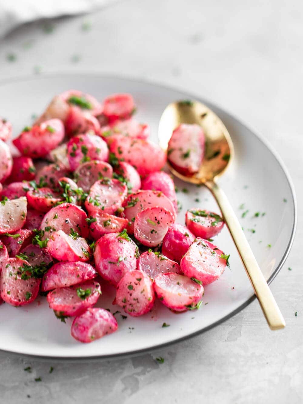 A plate of cooked radishes with fresh parsley and lemon juice drizzled on top.