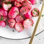 A plate of roasted radishes with fresh parsley and lemon juice drizzled on top.