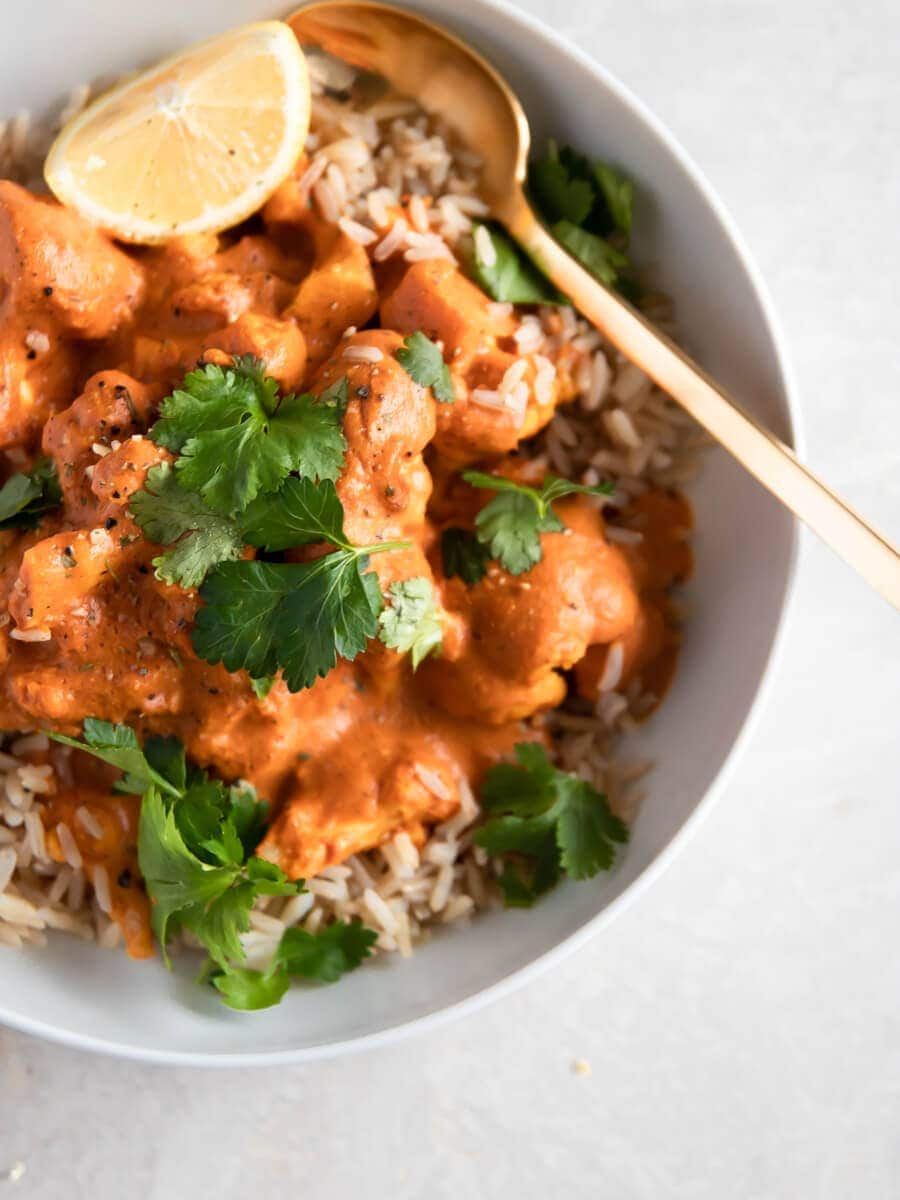 A bowl of vegan cauliflower tikka masala on a bed of Indian Basmati rice, topped with fresh cilantro and a wedge of lemon.