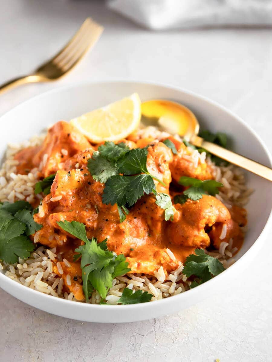 A bowl of  tikka masala on a bed of Indian Basmati rice, topped with fresh cilantro and a wedge of lemon.