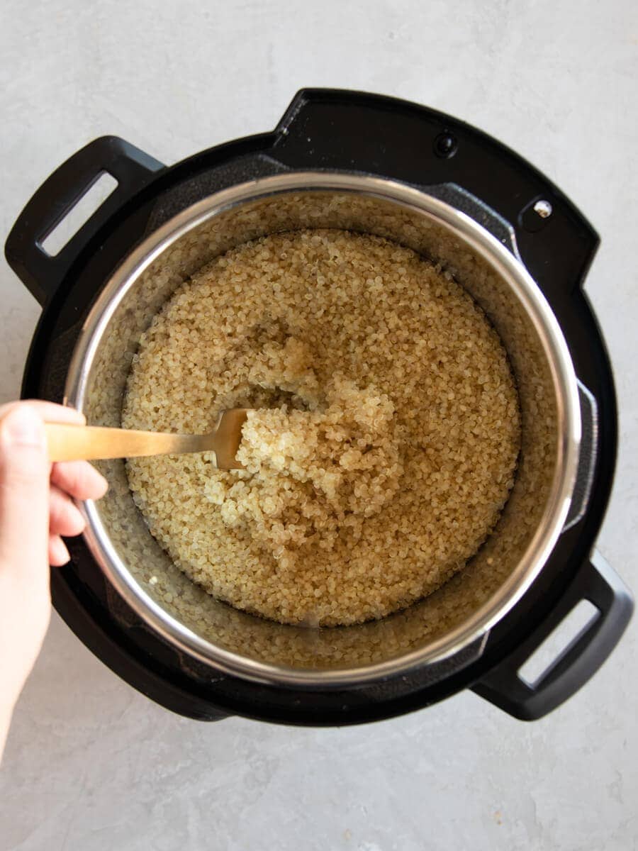 Hand using fork to fluff cooked quinoa.