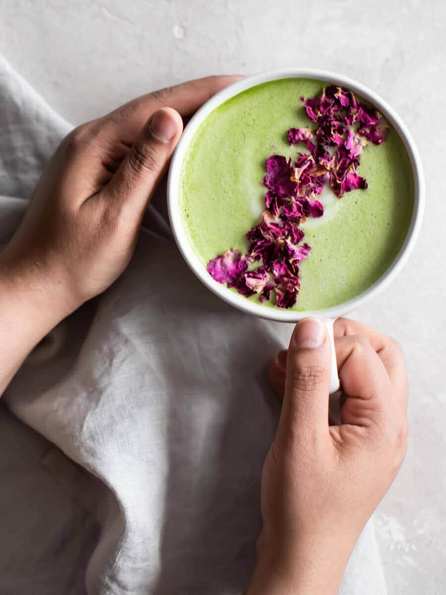 Hands holding a cup of matcha, sprinkled with dried rose petals.