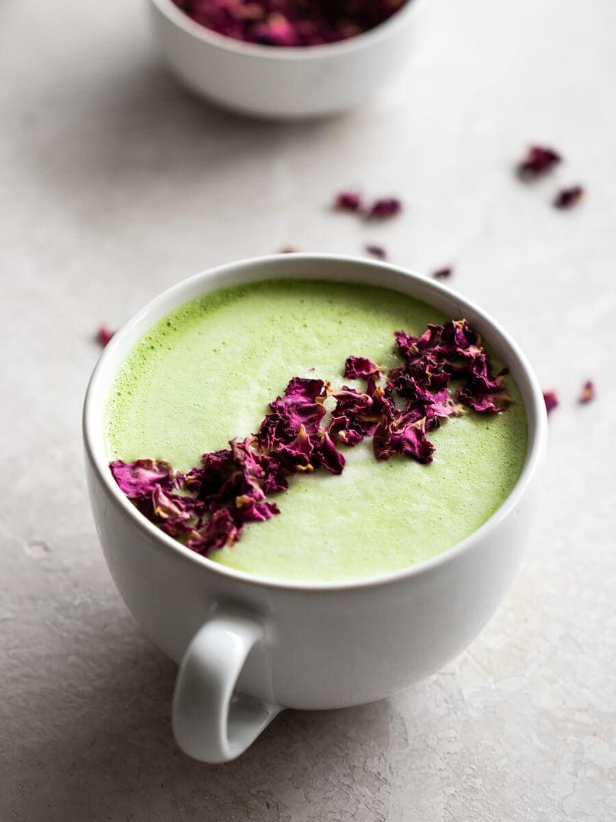 A cup of frothy matcha latte sprinkled with rose petals