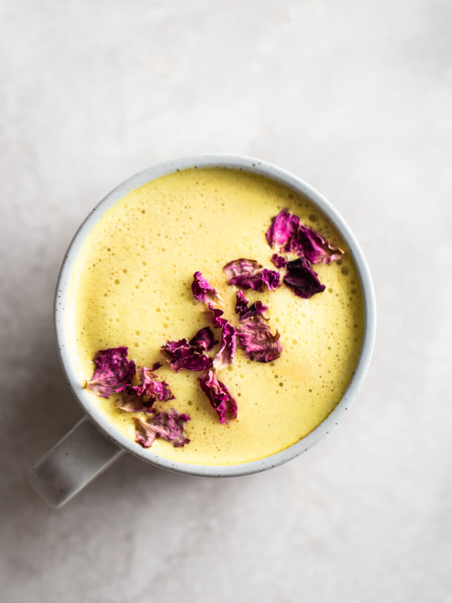 A cup of turmeric latte with rose petals sprinkled on top