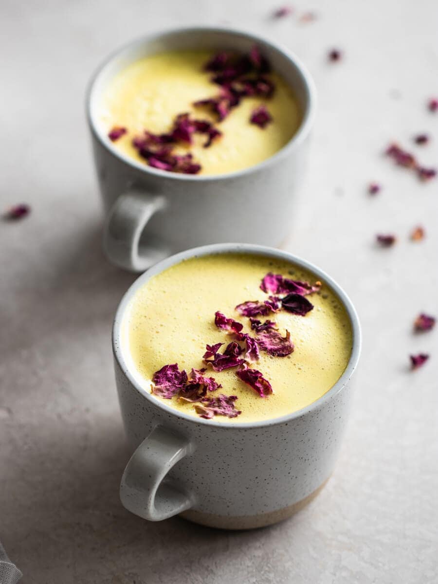 Two cups of turmeric milk, with dried rose petals sprinkled on top.