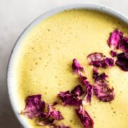 A cup of turmeric milk, with dried rose petals sprinkled on top.