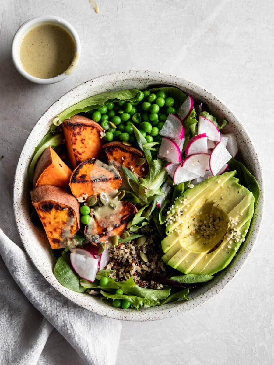 A vegan power bowl filled with roasted sweet potato, avocado, green peas, quinoa, fresh greens, and veggies.