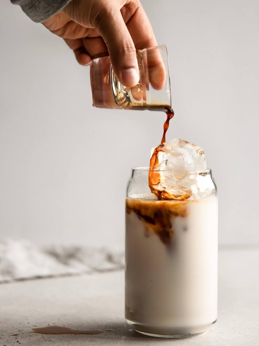 A glass of iced milk with a shot of espresso being poured into it. 
