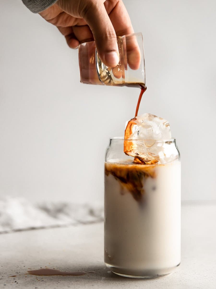 Pouring a shot of espresso into a glass of iced almond milk.
