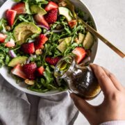 Hand drizzling vinaigrette on strawberry arugula salad