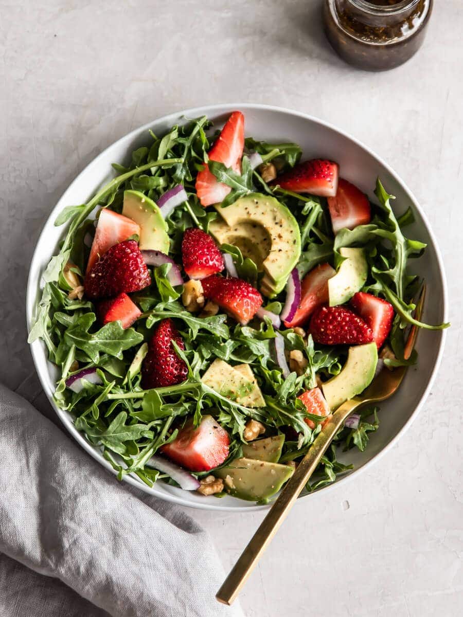 A bowl of strawberry arugula salad with balsamic vinaigrette.
