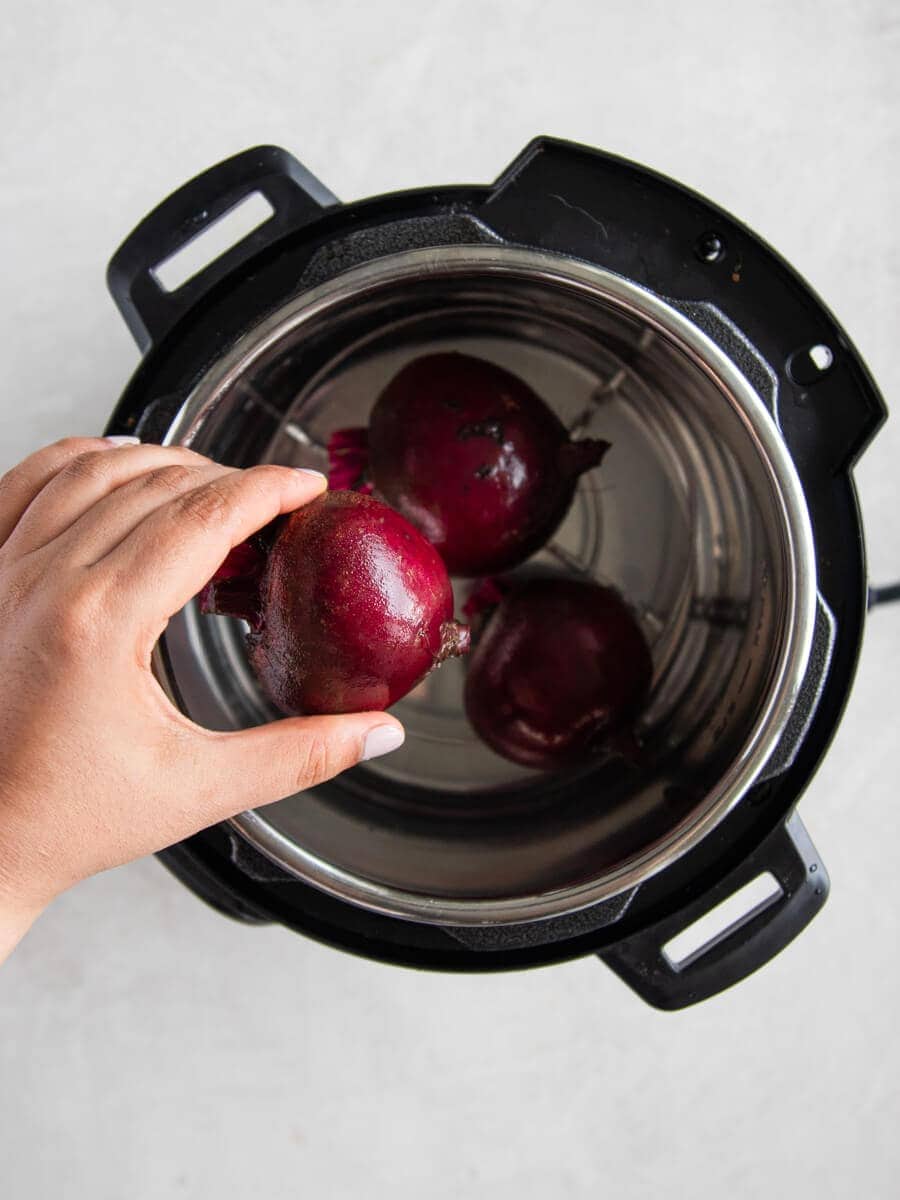 Hand placing beets on the rack inside the Instant Pot.