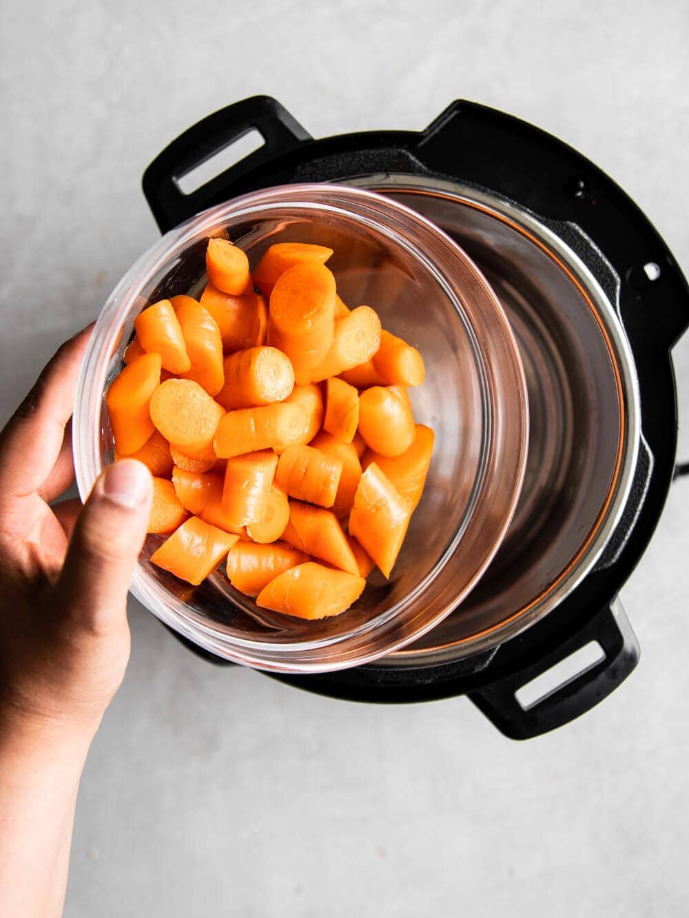 Hand pouring a bowl of chopped carrots into the insert of the Instant Pot.