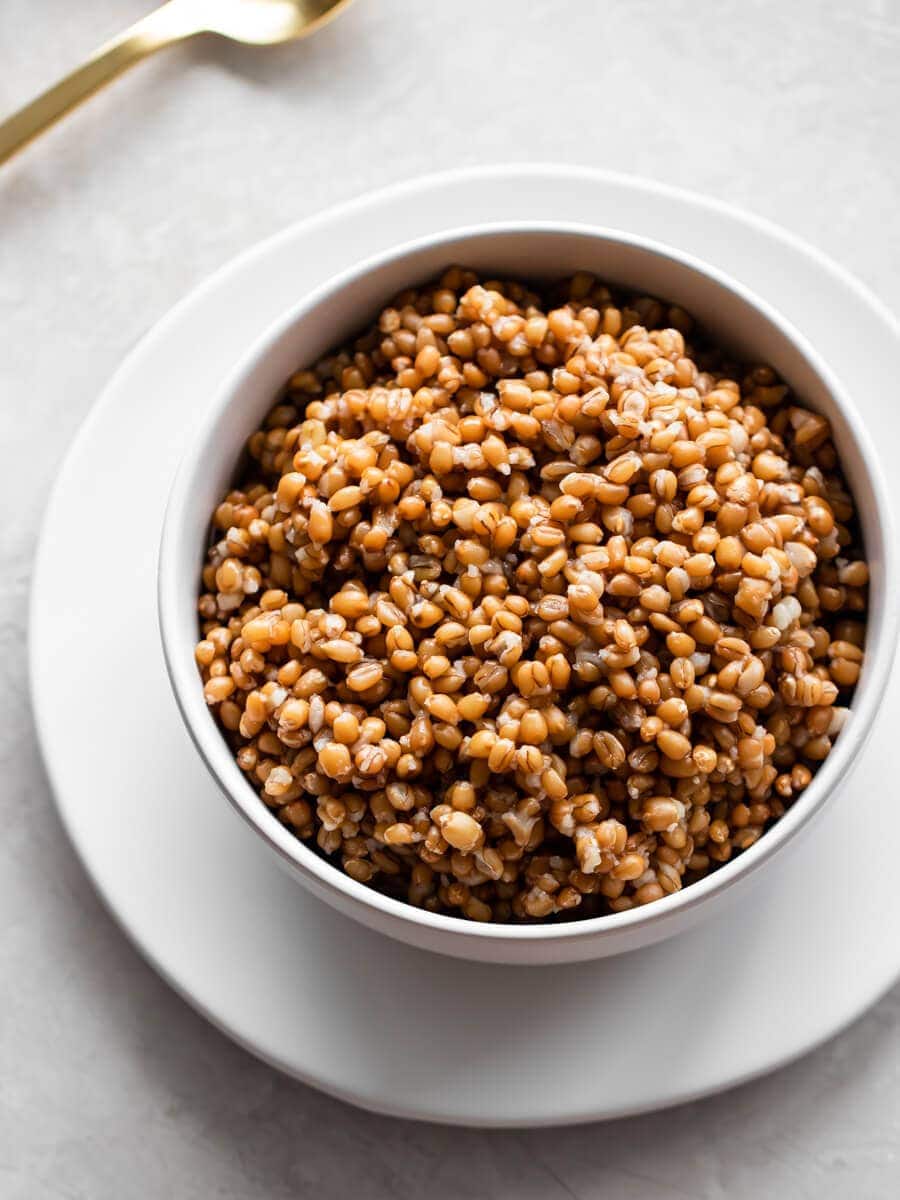 A bowl of cooked wheat berries with a spoon next to it.