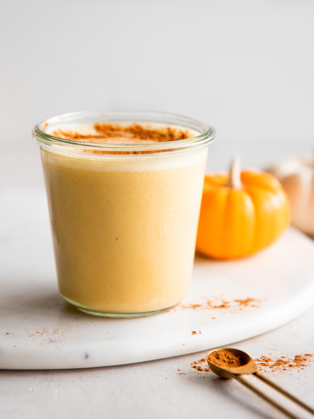 A glass of smoothie with two pumpkin in the background