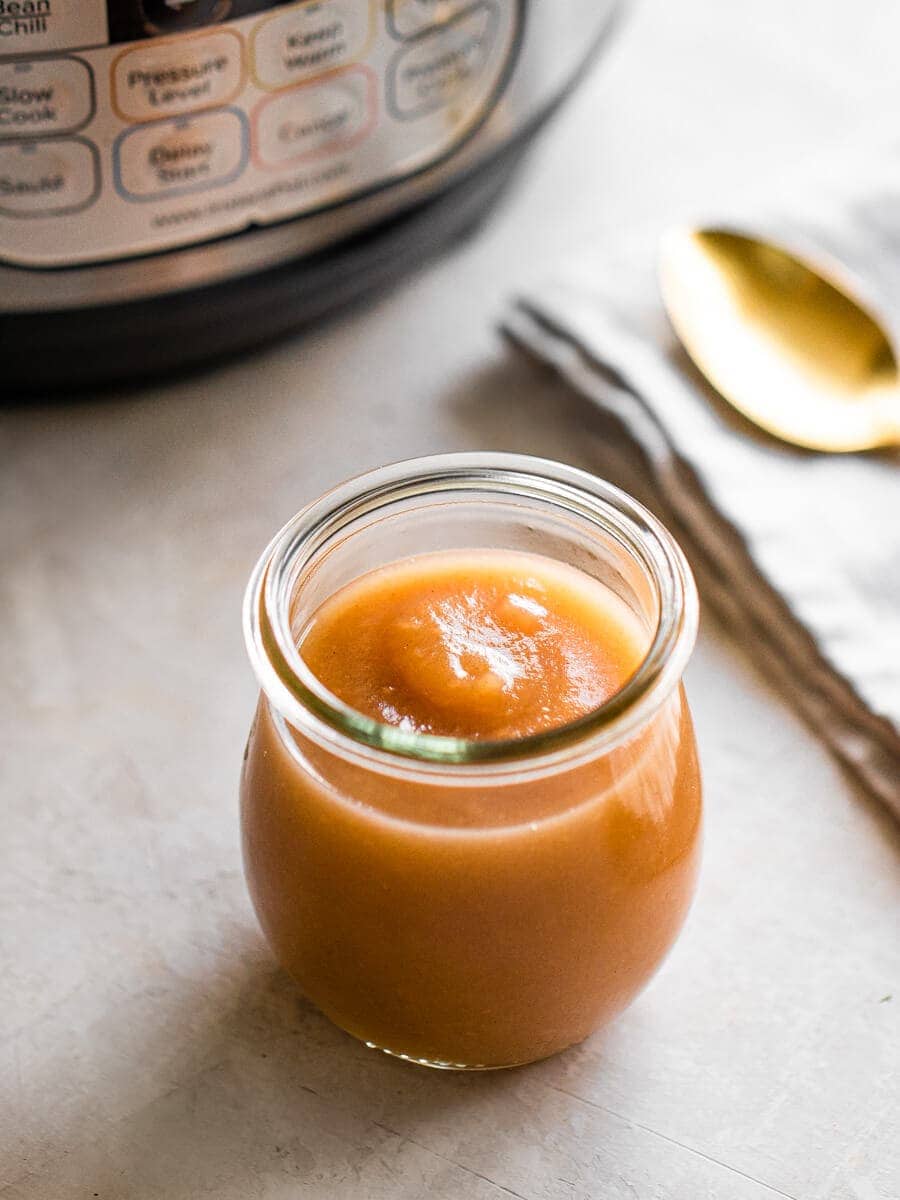 A jar of creamy apple butter in front of an Instant Pot