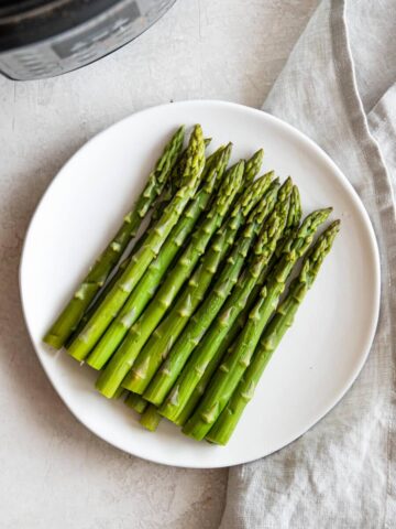 Plate of cooked asparagus with the Instant Pot in the corner.
