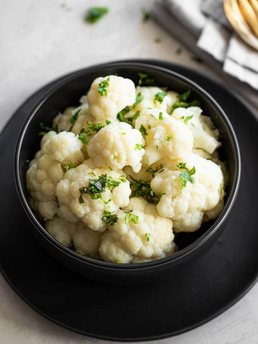 A bowl of steamed cauliflower with fresh herbs on top.