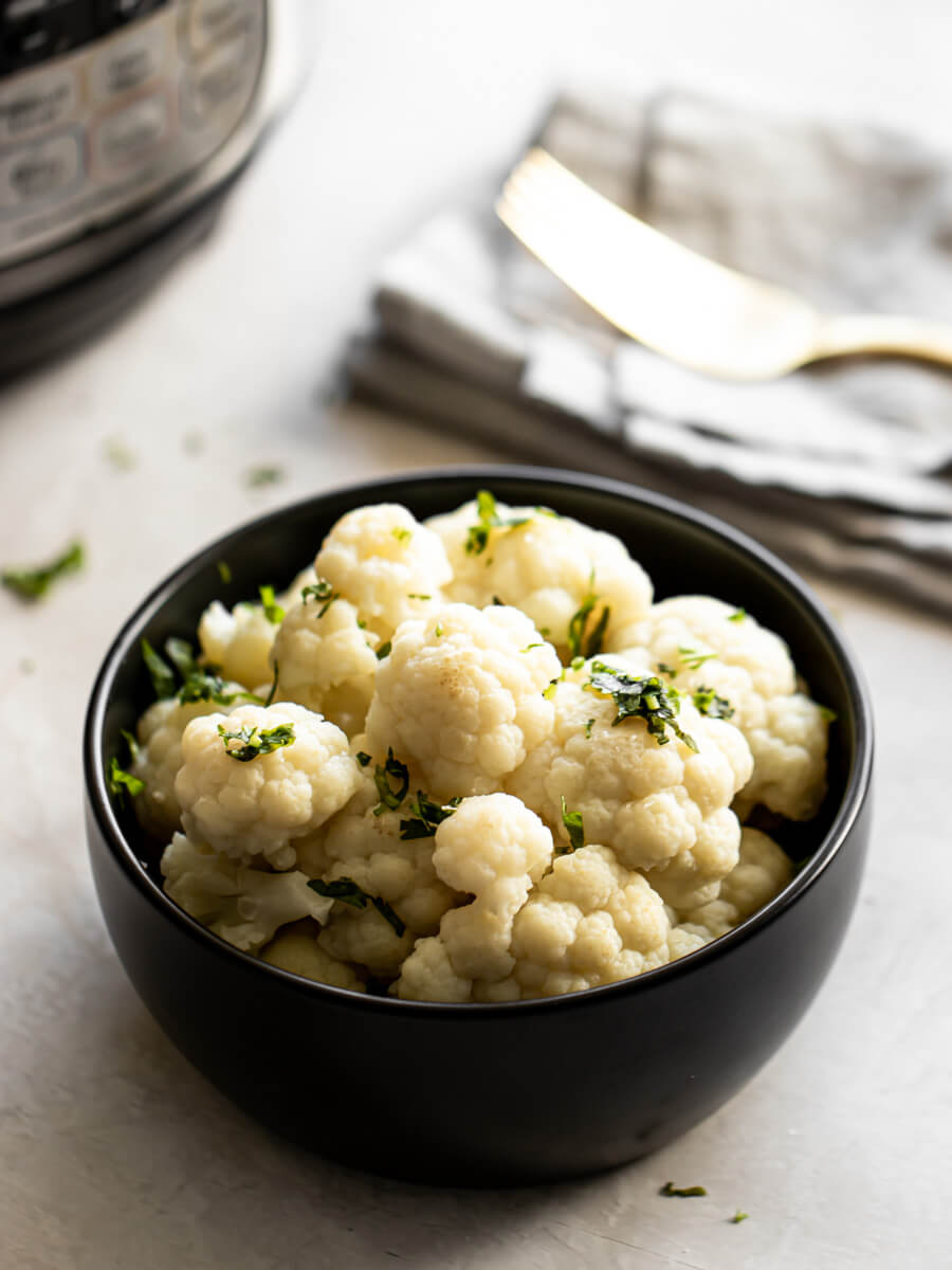 A bowl of Instant Pot Cauliflower in front of the Instant Pot and a fork.