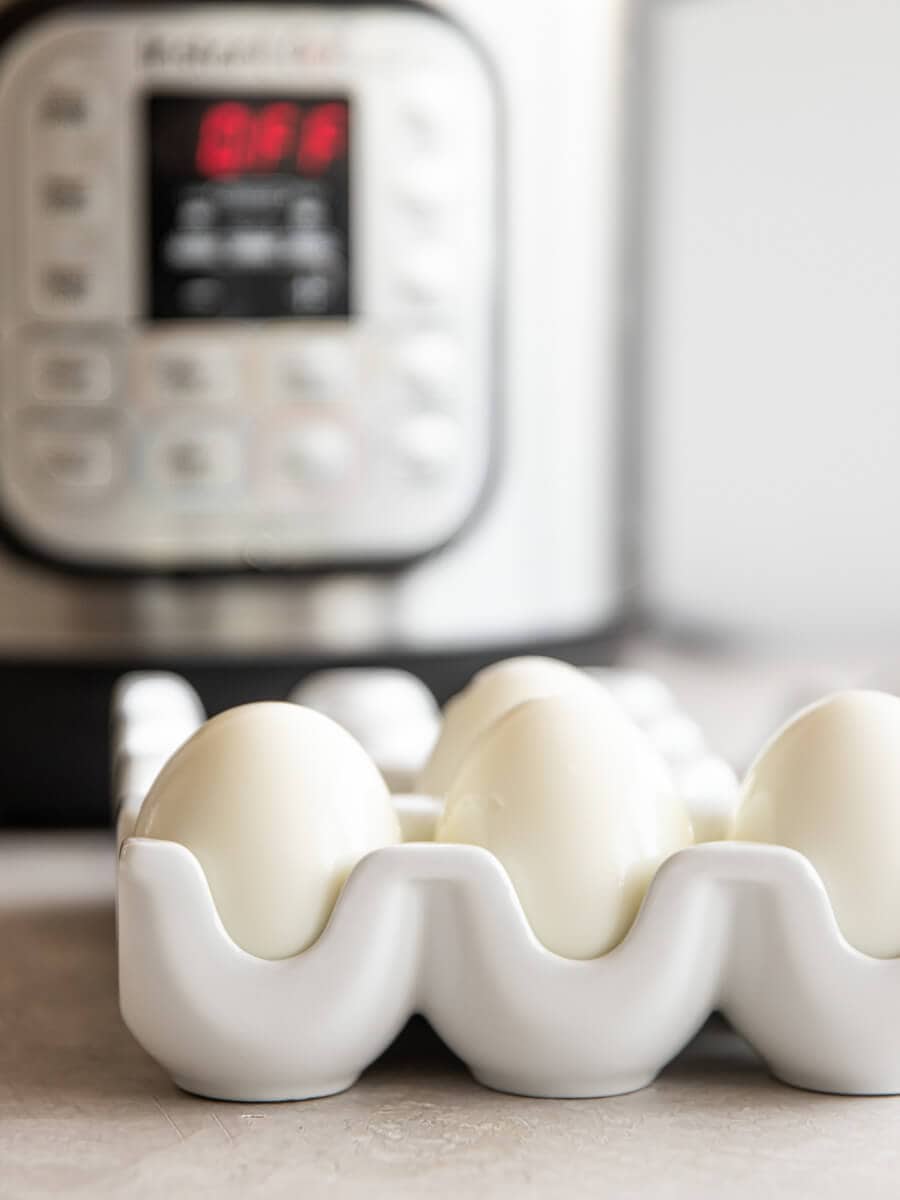 Four peeled hard-boiled eggs in a ceramic egg holder with the Instant Pot in the background.