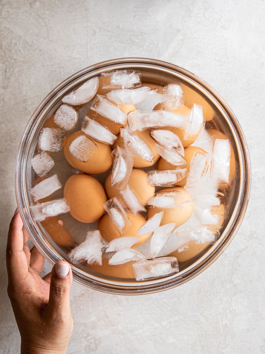 Hand holding a large glass bowl filled with eggs, ice, and water.