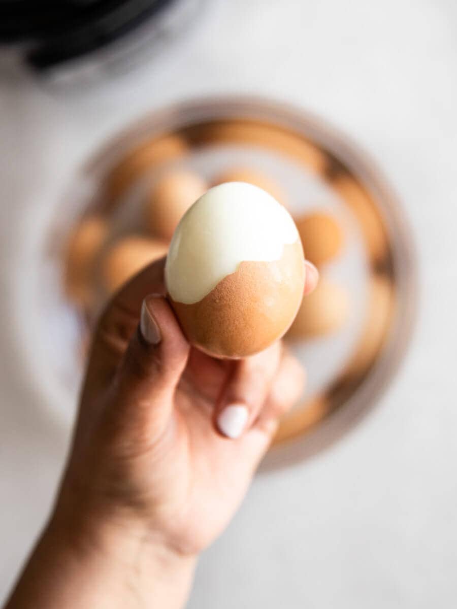 A hand holding a half-peeled hard boiled egg.
