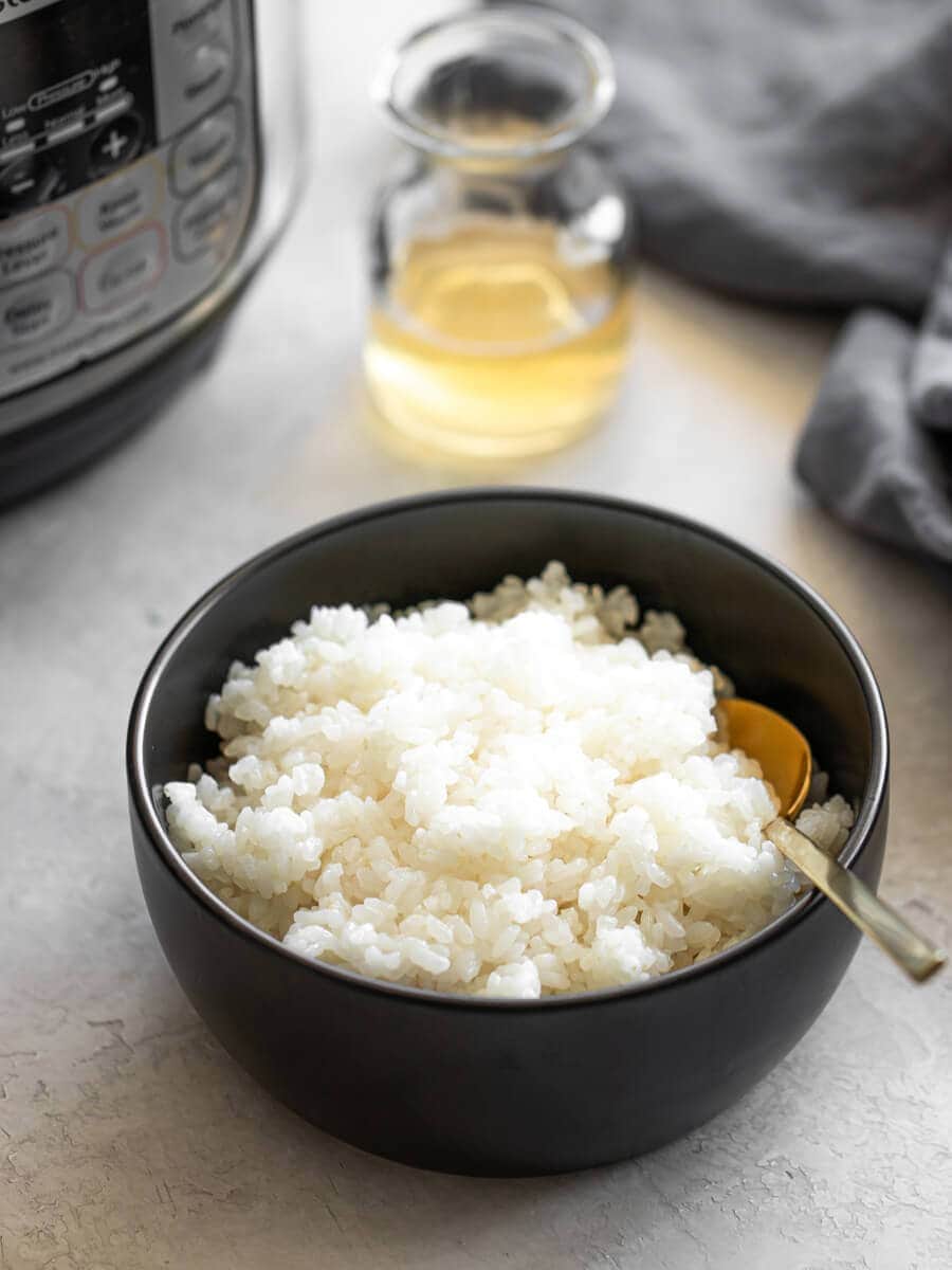 Bowl of sushi rice with a container of mixture in the back.