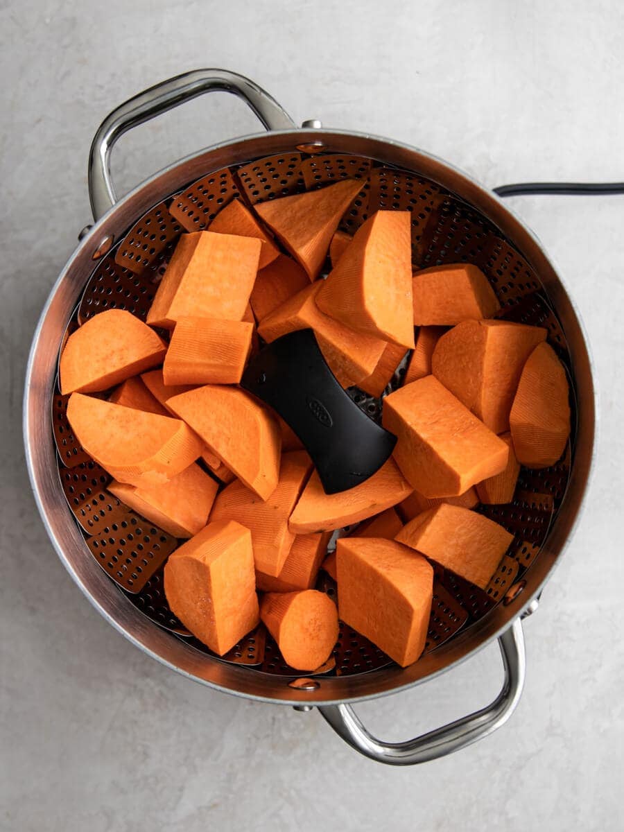 Big pot with diced sweet potatoes sitting on a steamer basket