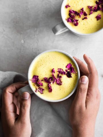 Two hands holding a cup of turmeric latte