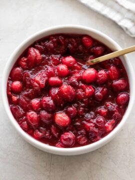 Bowl of cranberry sauce with golden spoon and napkin.