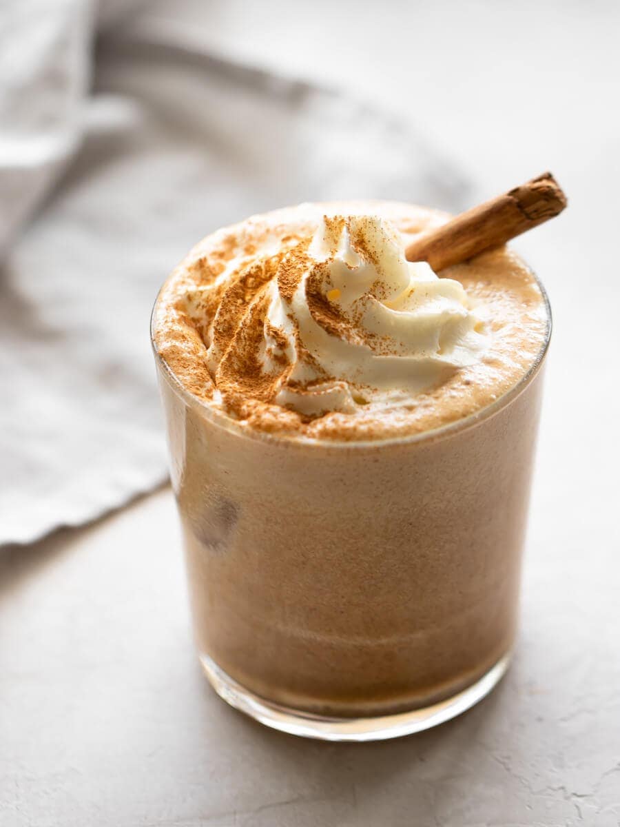 Glass of iced latte with whipped cream and a cinnamon stick on top.