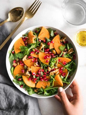 Hand holding persimmon salad with dressing on side.