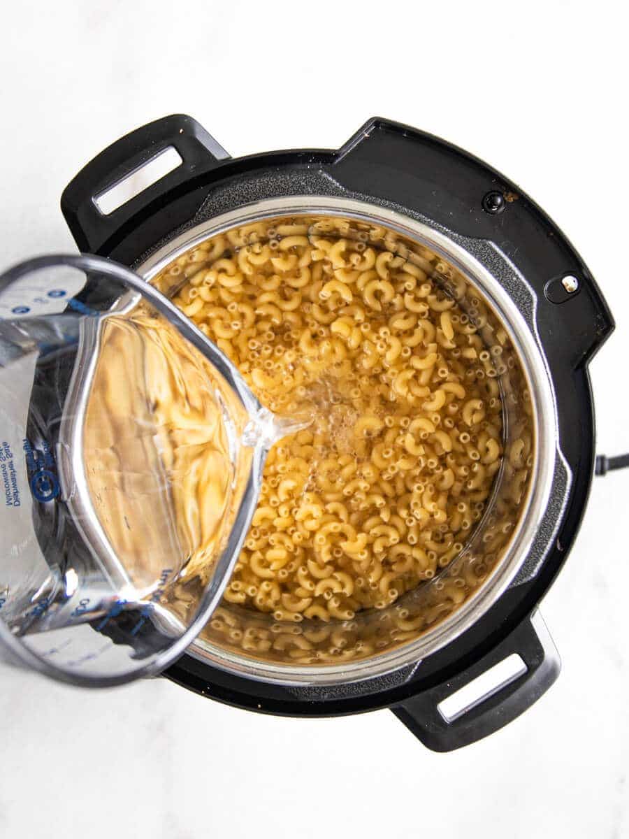 Water being poured into Instant Pot with pasta noodles