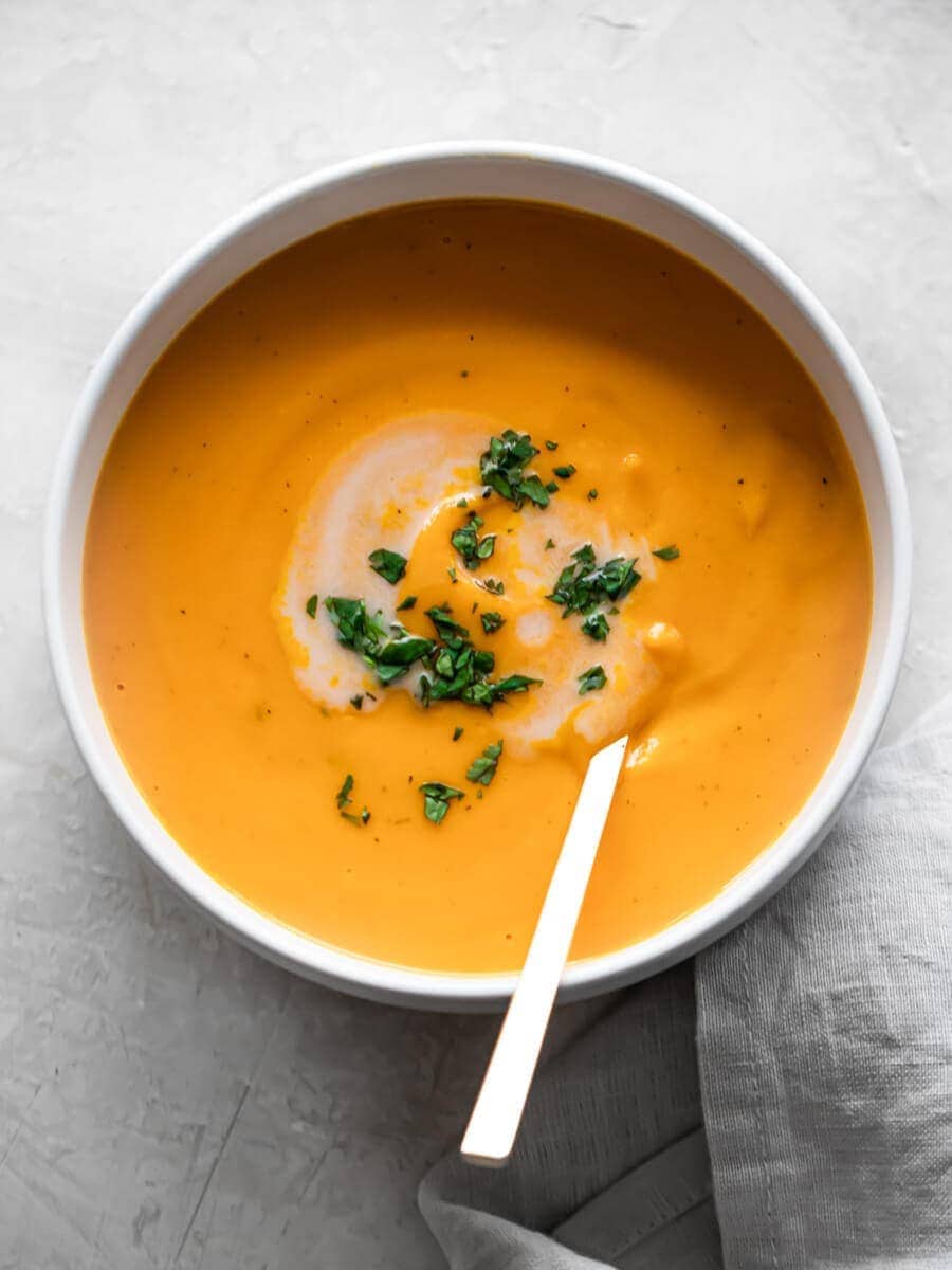 Bowl of sweet potato soup sprinkled with parsley and drizzled with coconut milk