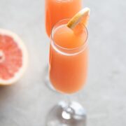Two glasses of grapefruit mimosa with a grapefruit on the side.