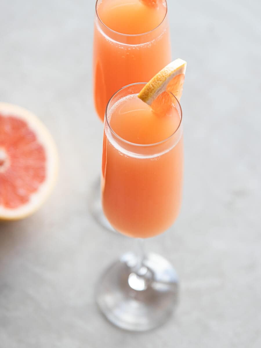Two glasses of grapefruit mimosa with a grapefruit on the side.