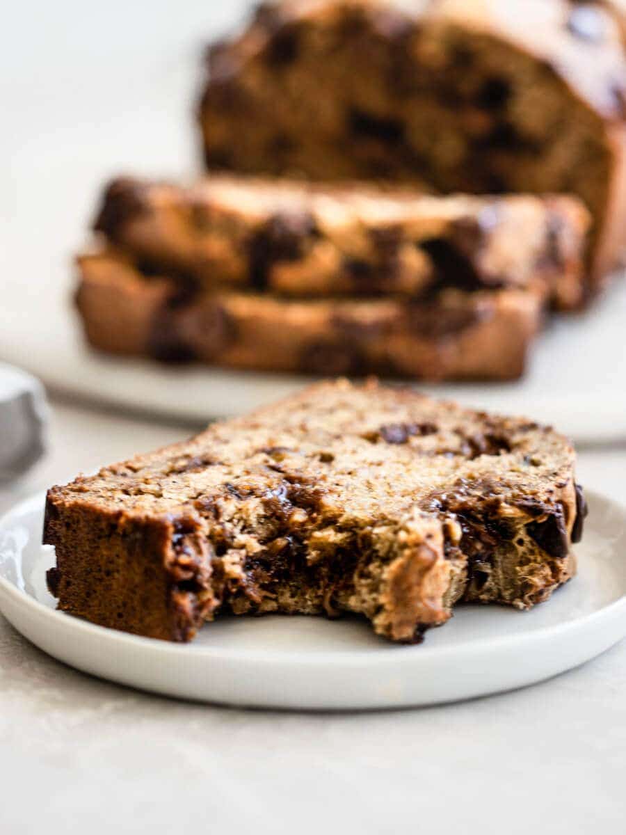 A slice of banana bread with a bite taking sitting on a plate.