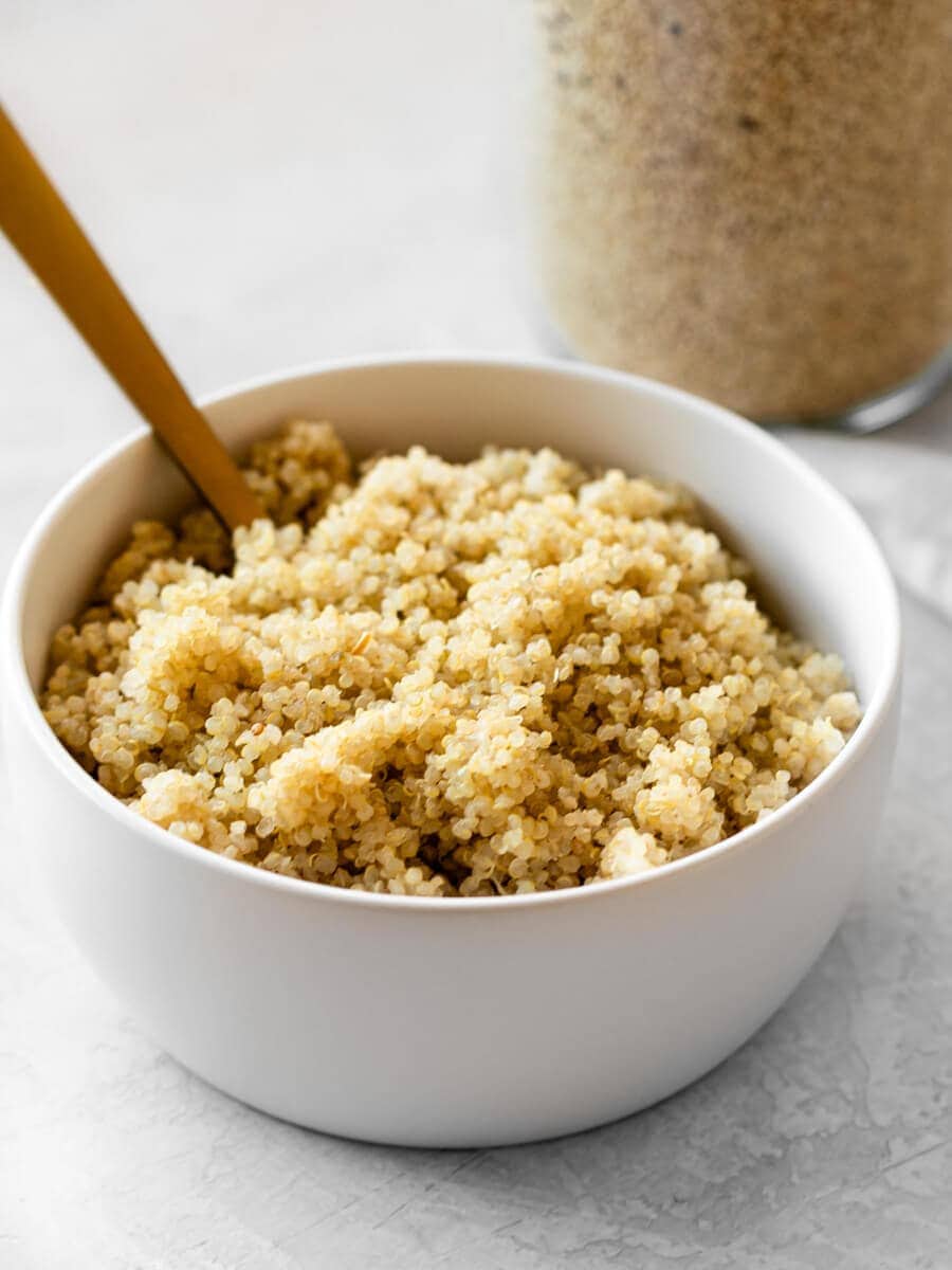 Bowl of cooked quinoa with a glass container behind it.