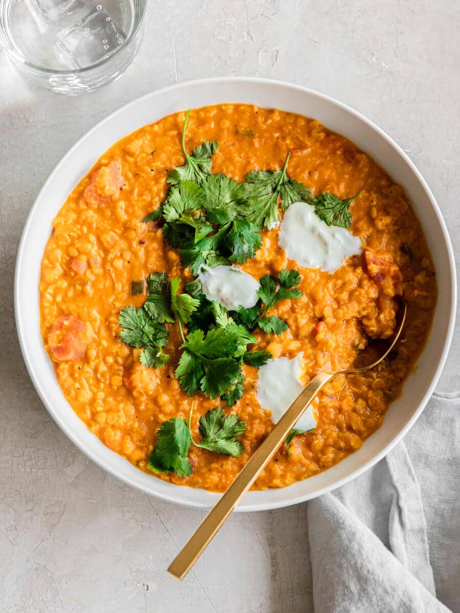 Bowl of red lentil. curry with a glass of iced water next to it.