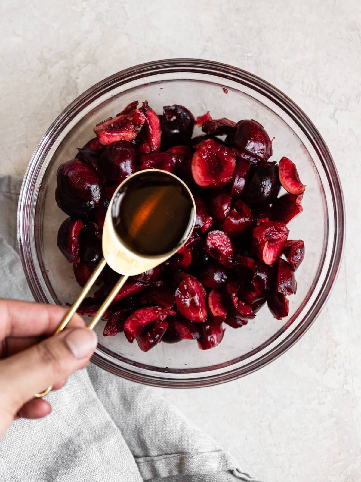 Hand pouring maple syrup into a bowl of cherries.